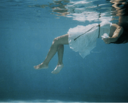 Menina submersa em uma piscina. Piscinas rasas não suportam saltos de ponta.