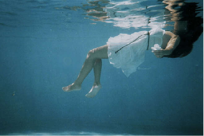 Menina submersa em uma piscina. Piscinas rasas não suportam saltos de ponta.